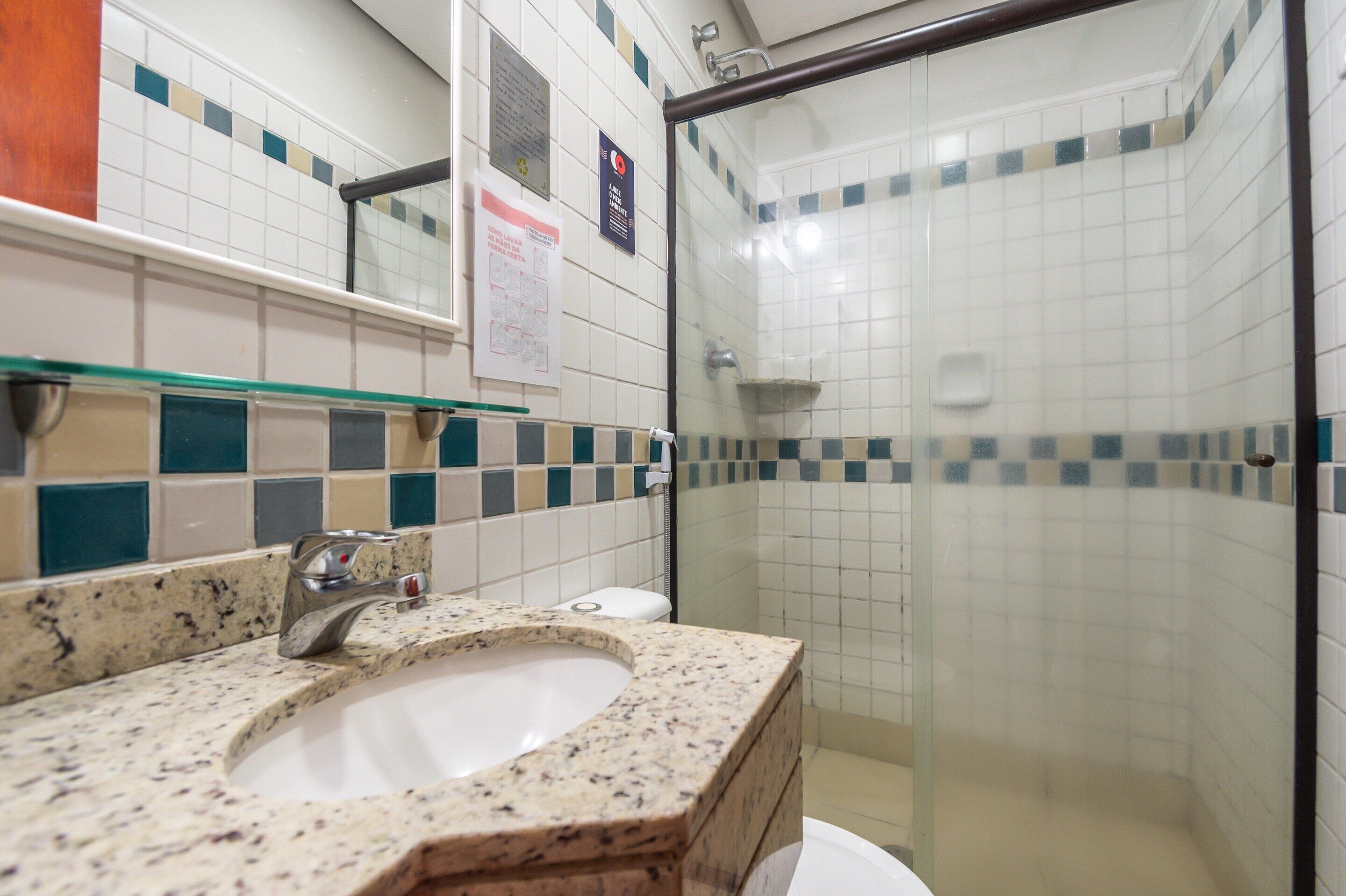 Un baño con lavamanos de granito, cabina de ducha con mampara de vidrio y paredes revestidas con azulejos.