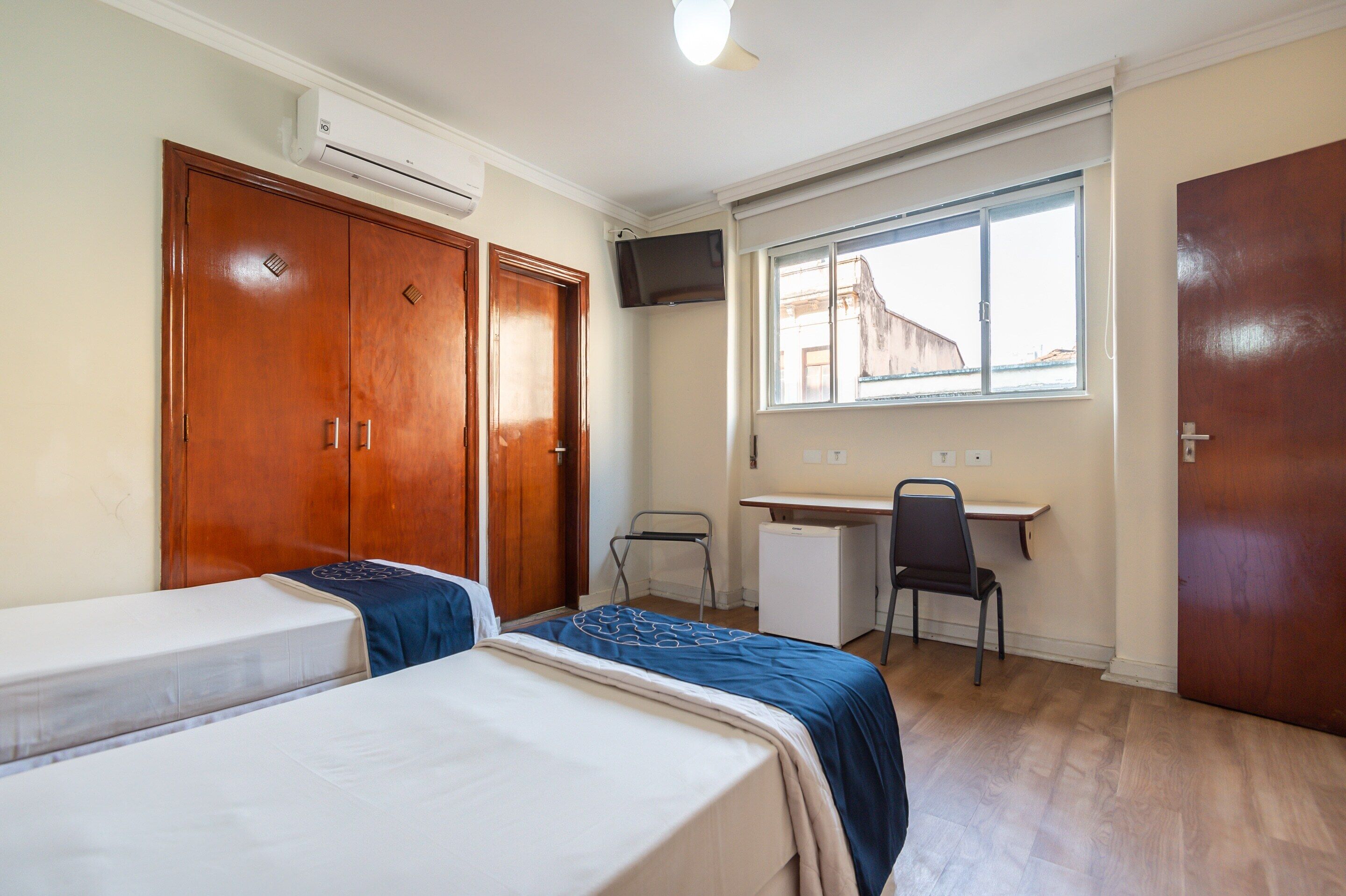A bedroom with two beds, a desk, a chair, and a window with a view.