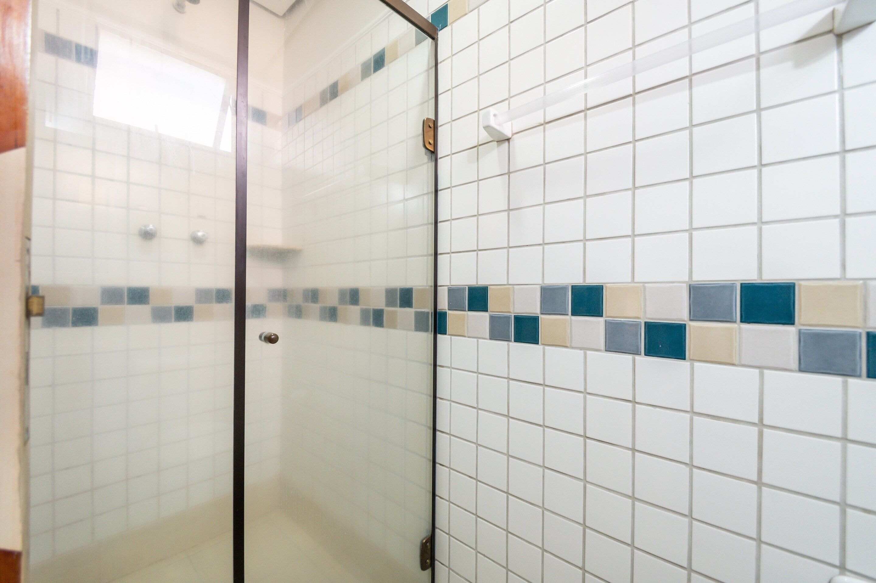 A bathroom with white tiles and a glass shower enclosure.