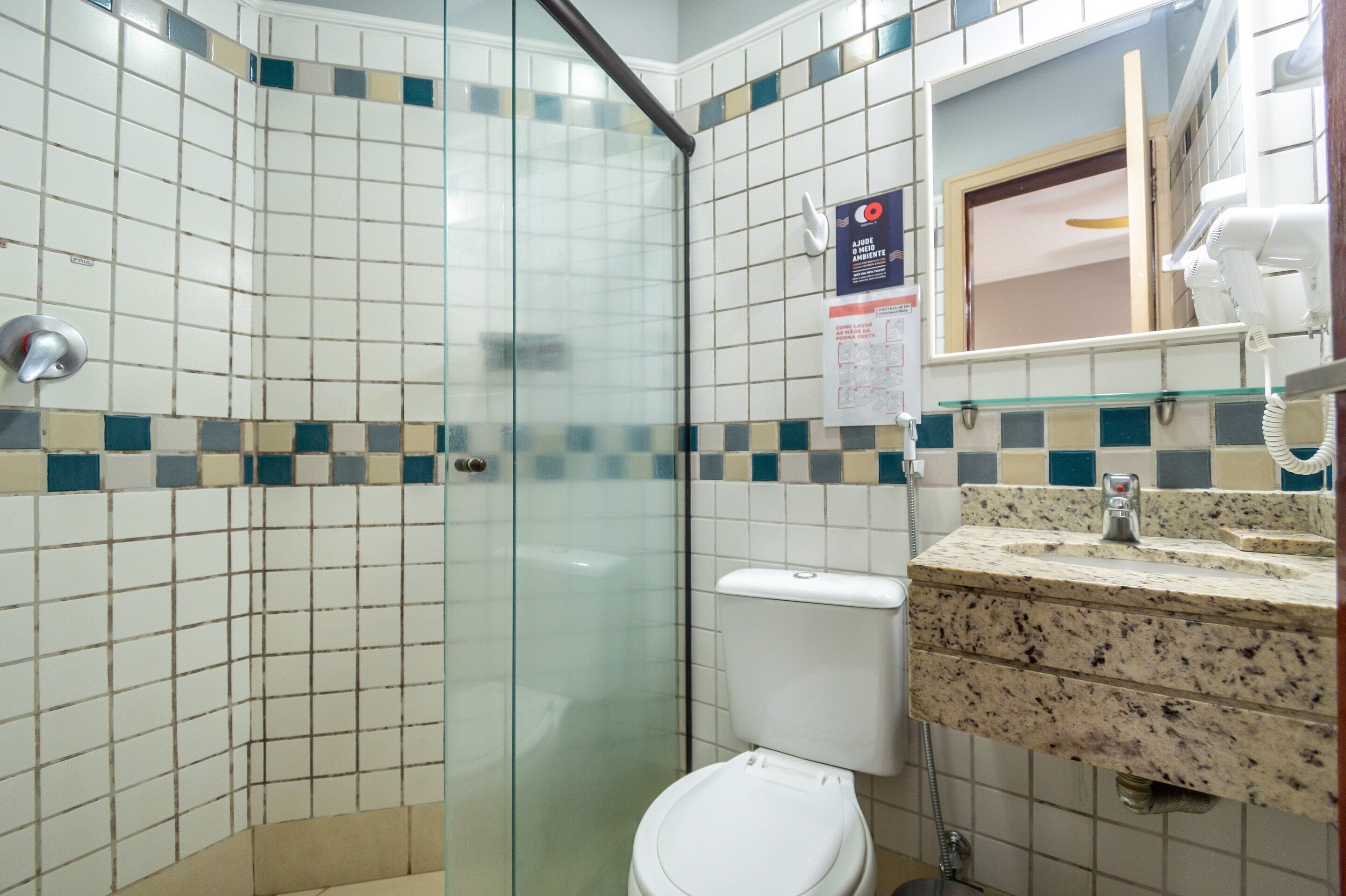 A bathroom with a glass-enclosed shower, a white toilet, and a granite countertop sink with a mirror above it.