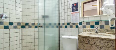 A bathroom with a glass-enclosed shower, a white toilet, and a granite countertop sink with a mirror above it.