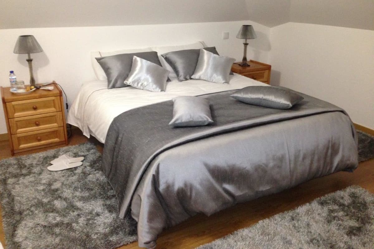 Ein Schlafzimmer mit einem Bett, zwei Nachttischen, einer Lampe auf jedem Nachttisch, einem grauen Teppich und einer Holzkommode.
