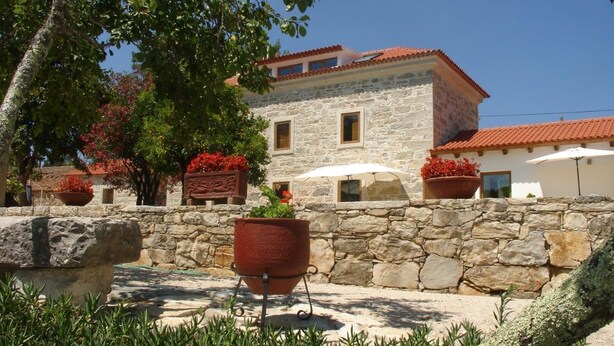 A stone building with a red-tiled roof, surrounded by potted plants and a white umbrella. - Otium Country House (Ansiao)