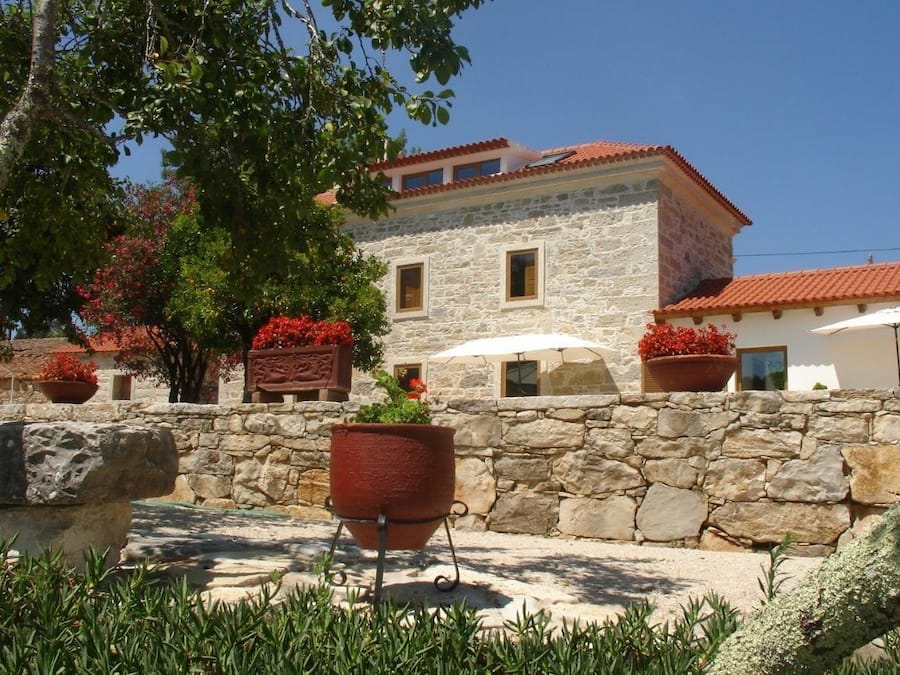A stone building with a red-tiled roof, surrounded by potted plants and a white umbrella.