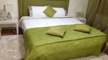 A neatly made bed with green bedding, white pillows, and a green throw pillow. There are two bedside tables with lamps and a white fluffy rug.