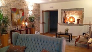 A living room with a blue sofa, a wooden coffee table, and a stone wall. There are potted plants and a guitar wall decoration. - Otium Country House (Ansiao)
