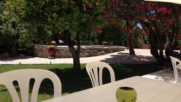 Eine Außenpatio mit weißen Stühlen und einem Tisch, umgeben von üppigem Grün und blühenden Bäumen.
