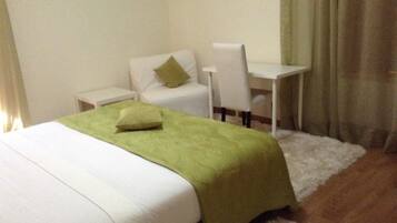 A hotel room with a bed, a desk, a chair, and a white rug.