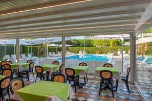 Ein Außenbereich zum Essen mit Tischen, Stühlen, einem Pool und Sonnenschirmen.