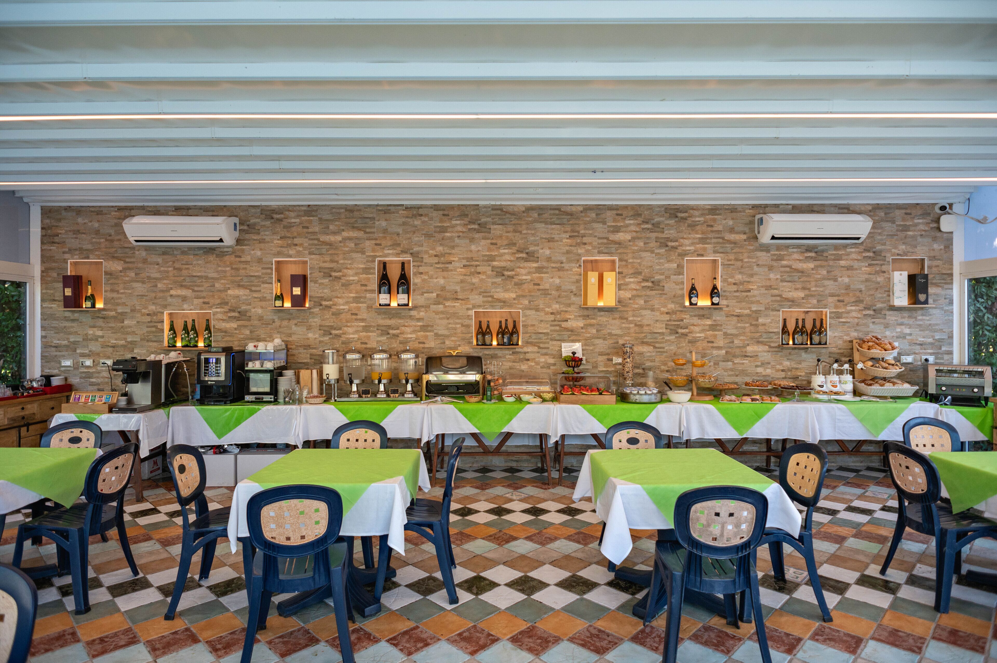 A restaurant with multiple tables and chairs, a stone wall, and various food and drink displays.