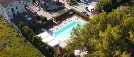 An aerial view of a residential property with a swimming pool, multiple buildings, and surrounding greenery.