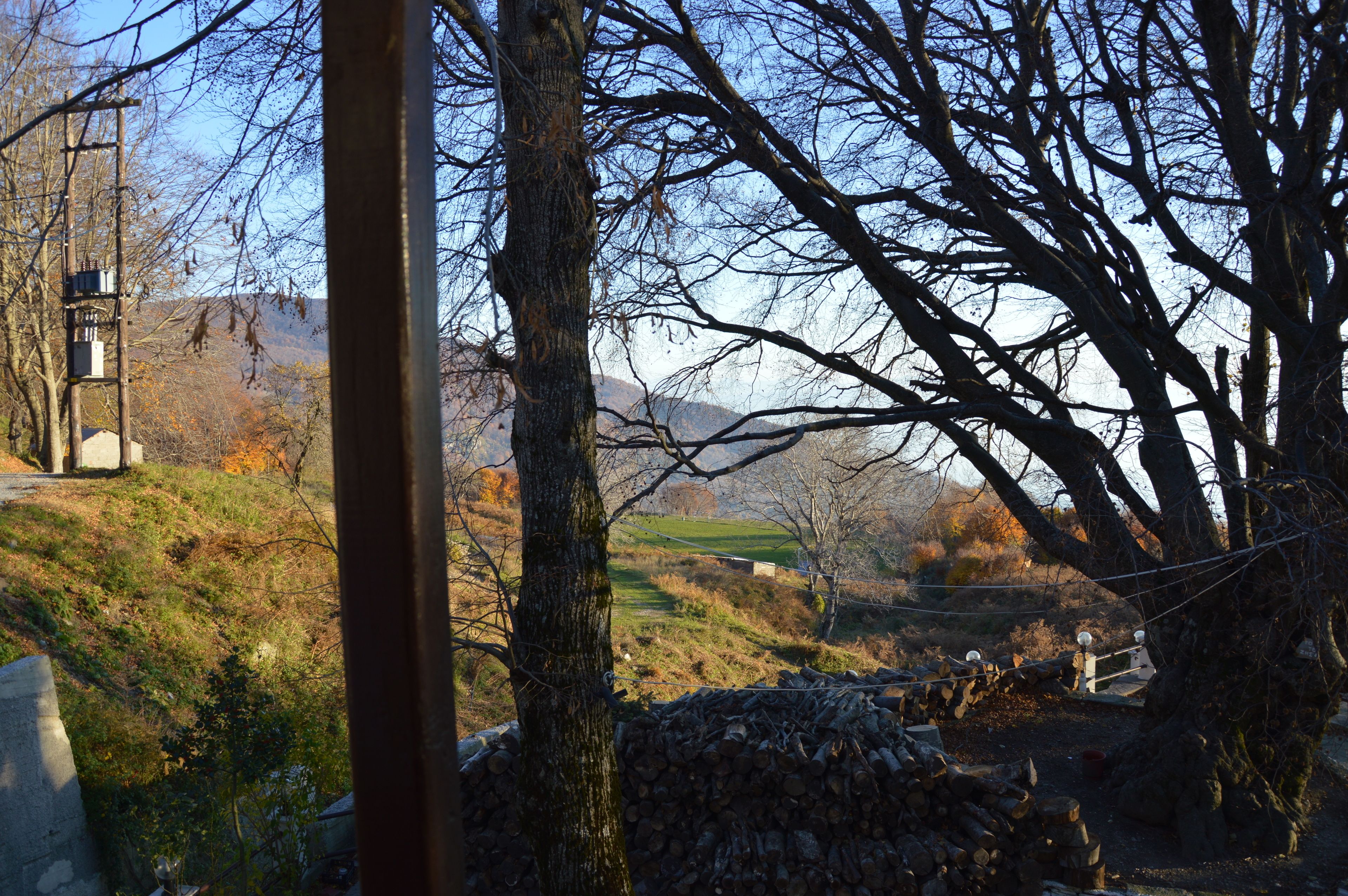 Paisaje rural con un muro de piedra, árboles y una vista distante de colinas.
