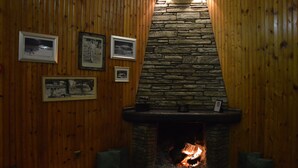 A cozy room with a stone fireplace, wooden walls, and framed pictures. - Hani Zisi Hotel (Volos)