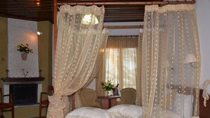 A four-poster bed with sheer curtains, a bedside table with a lamp, and a vase with flowers. - Hani Zisi Hotel (Volos)