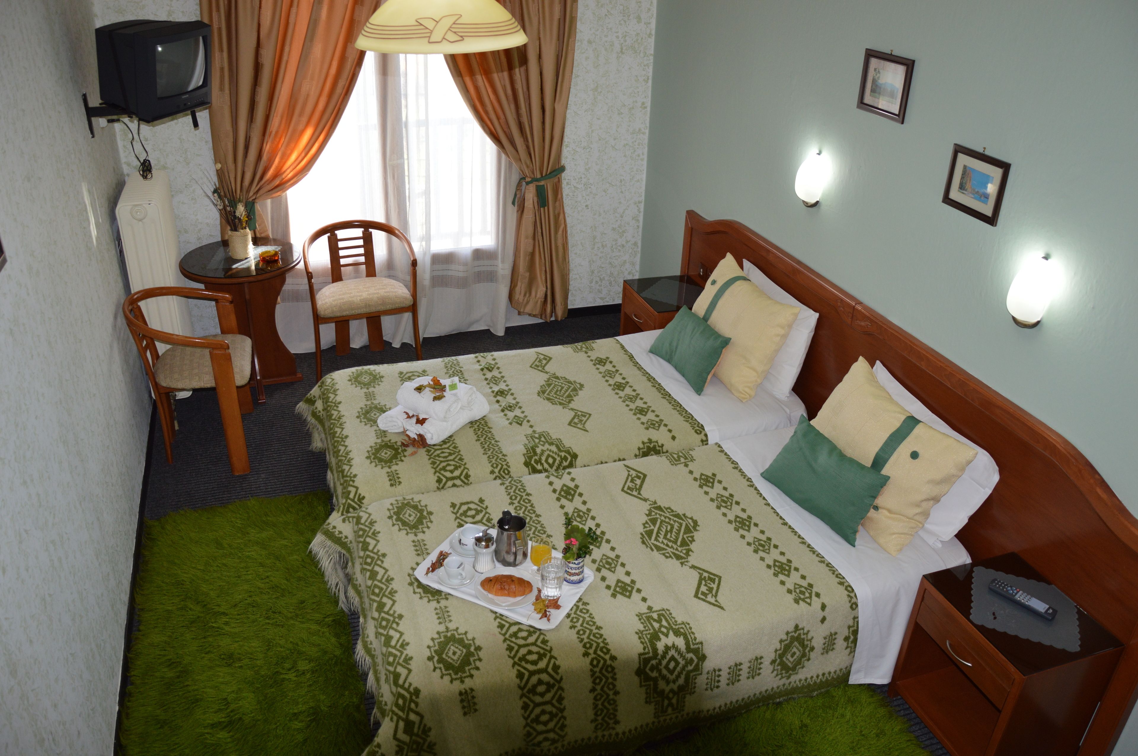 Habitación de hotel con cama, dos sillas, una mesita con lámpara, televisión y ventana con cortinas.