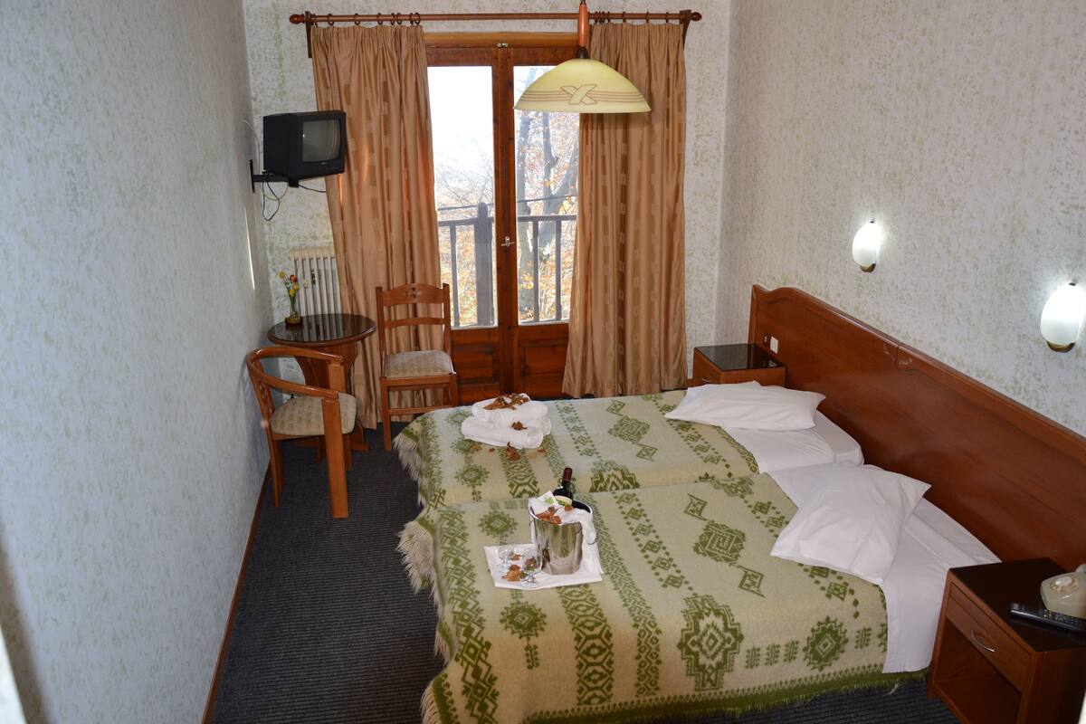 Una habitación de hotel con cama, escritorio, silla, televisión y ventana con cortinas.