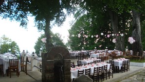 An outdoor dining area with stone flooring, tables set with white tablecloths and pink decorations, and trees in the background. - Hani Zisi Hotel (Volos)