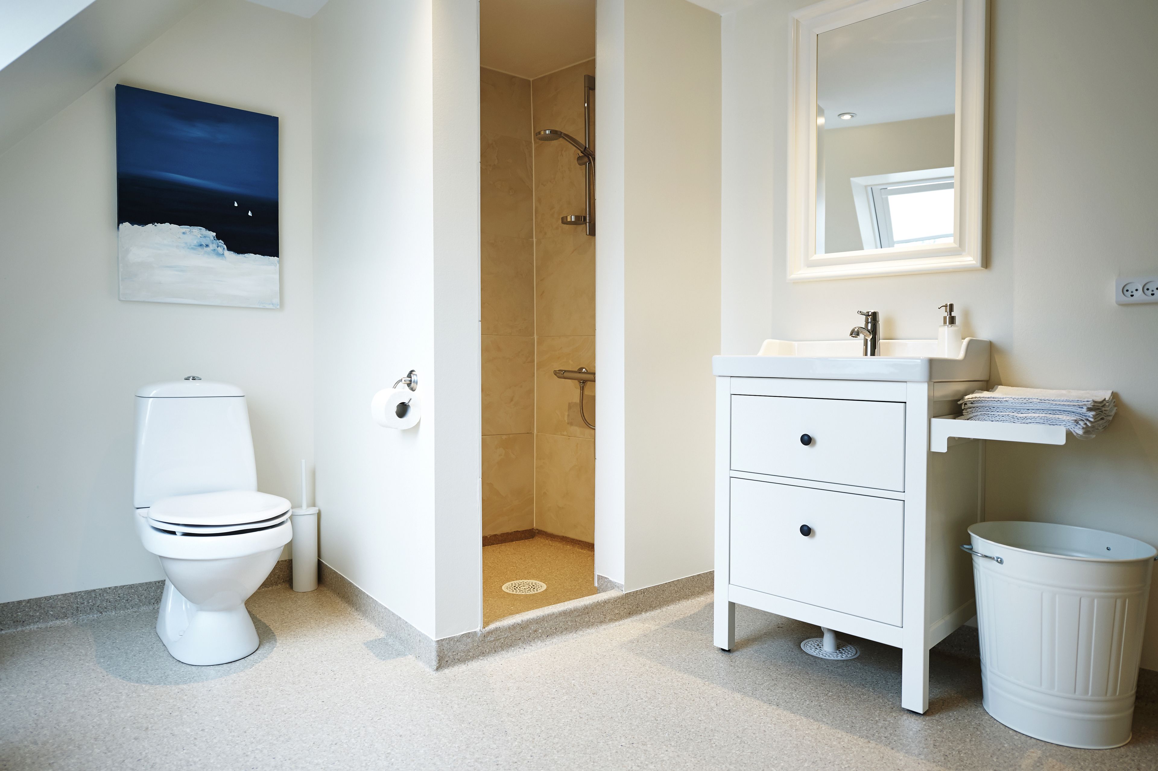 A modern bathroom with a toilet, shower, sink, and a painting of a night scene.