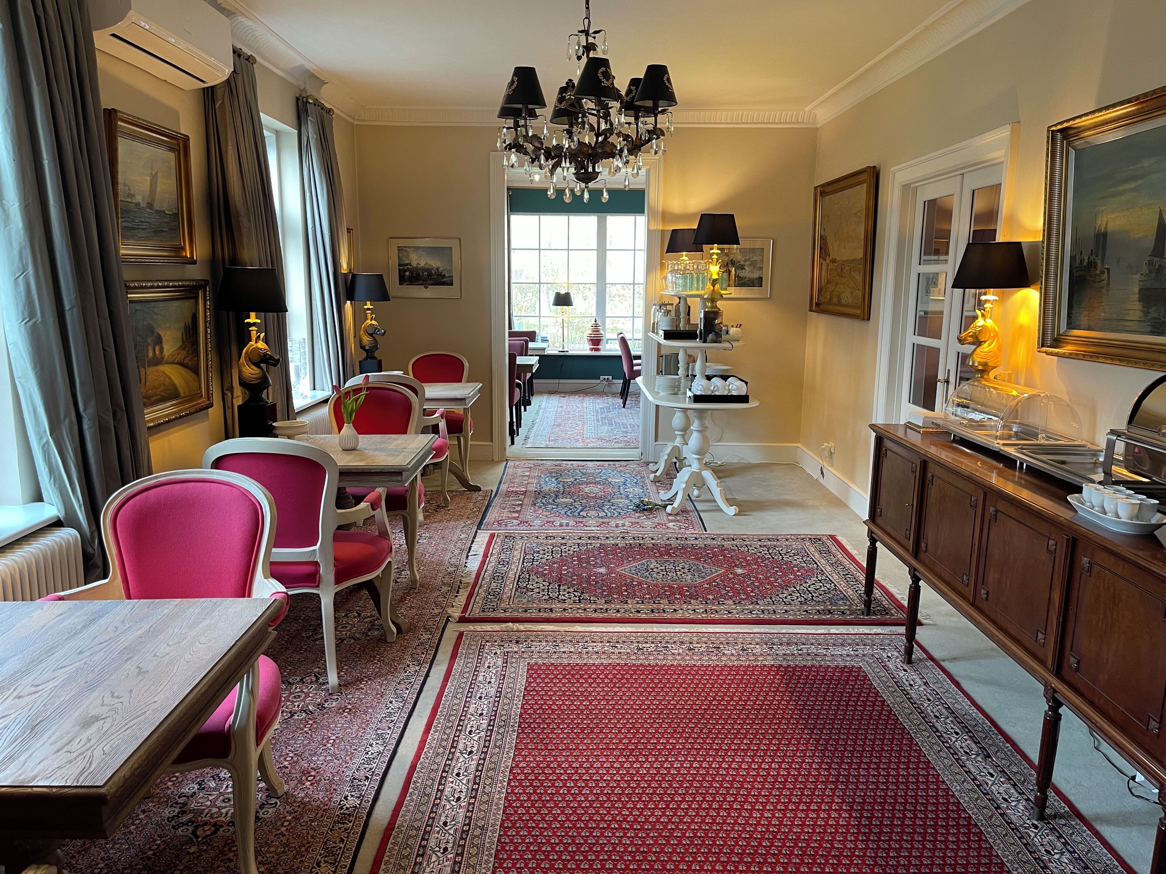 A dining area with red chairs, a wooden table, a chandelier, and a buffet with food items.