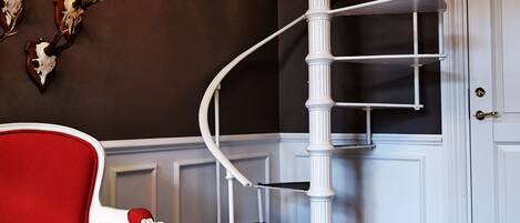 A spiral staircase with white railings, a red chair, and antler wall decorations.