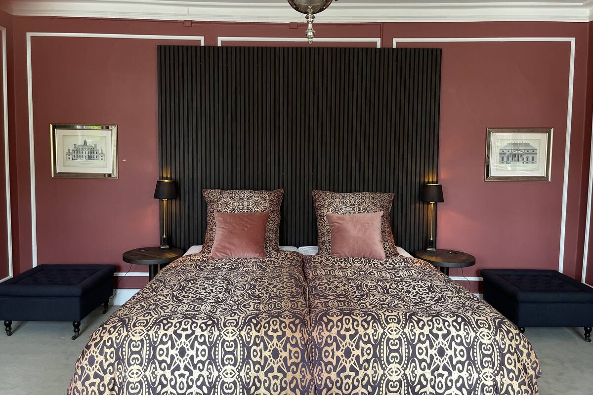 Une chambre à coucher avec un grand lit, deux tables de chevet, un lustre et des tableaux encadrés accrochés aux murs.