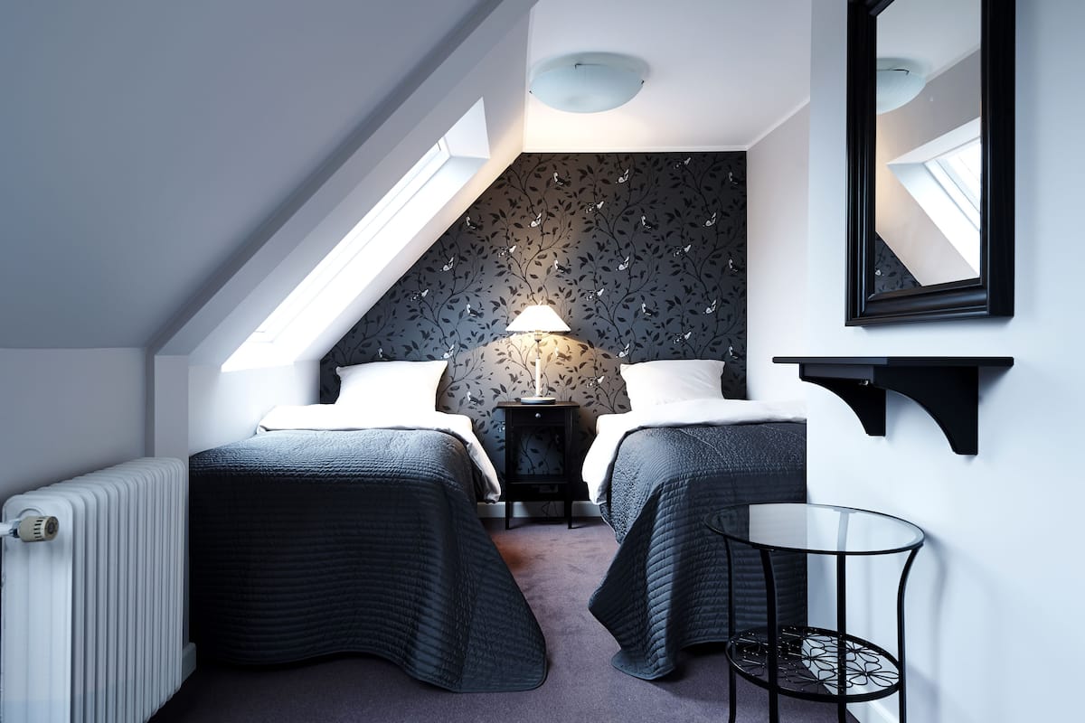 Une chambre moderne avec un plafond en pente, deux lits, une petite table, une lampe et un miroir.