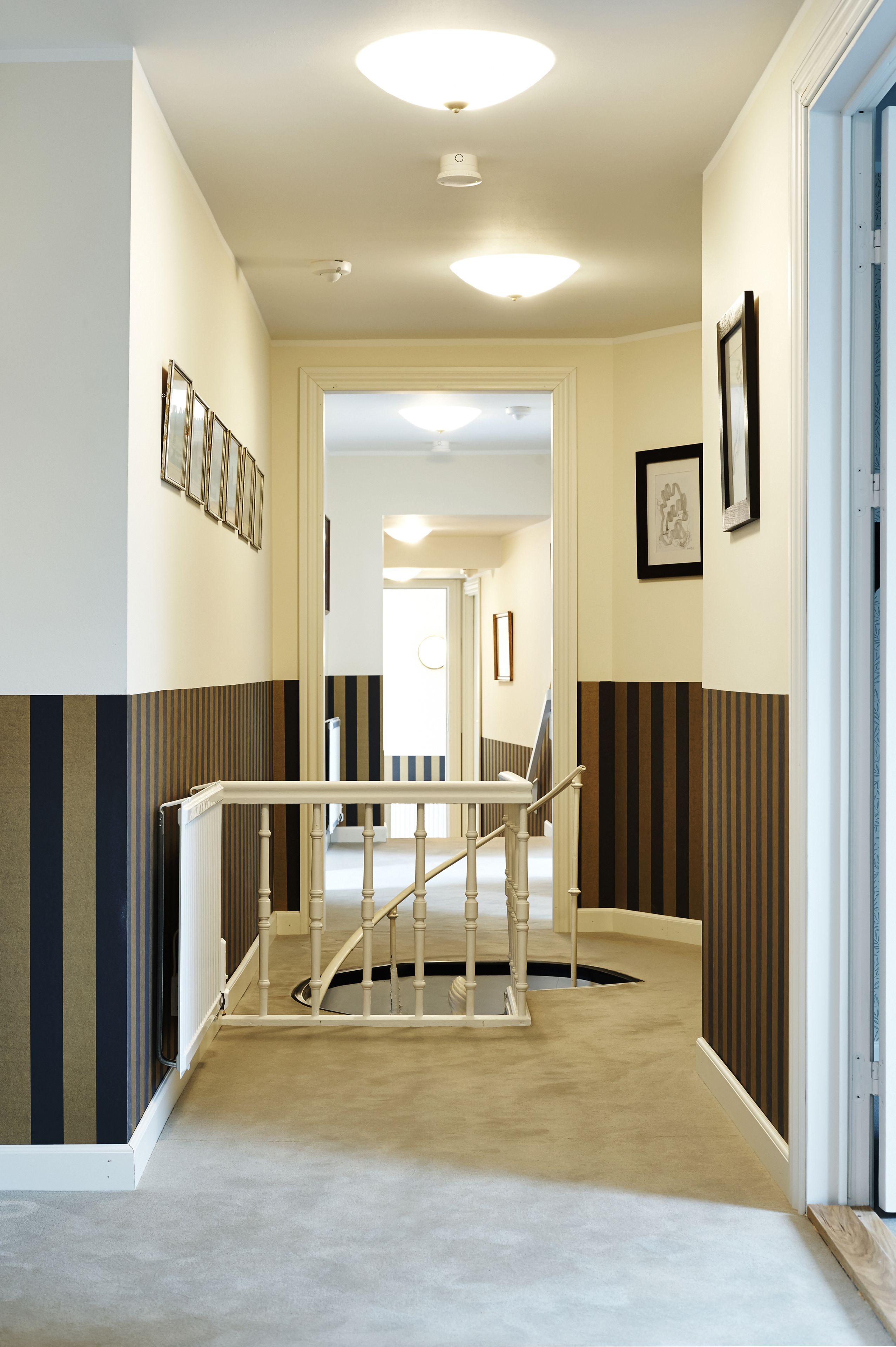A hallway with a carpeted floor, a wooden handrail, and framed pictures on the walls.