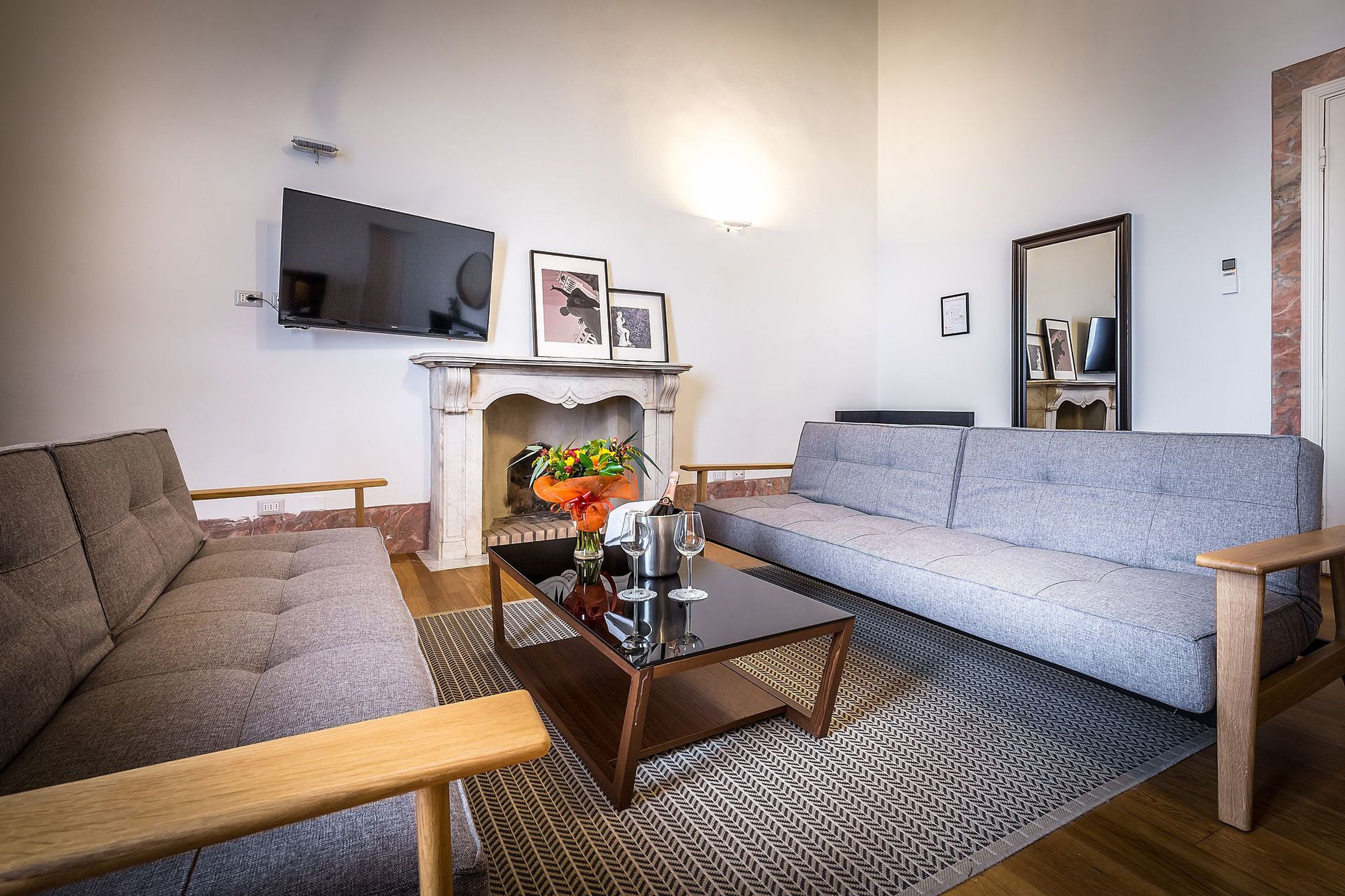 A living room with a grey sofa, a wooden coffee table, a fireplace, and a flat-screen TV mounted on the wall.