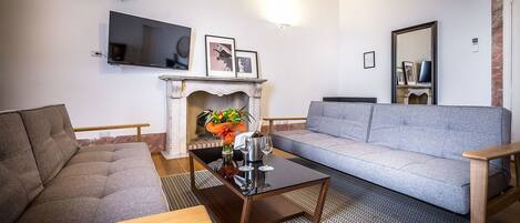 A living room with a grey sofa, a wooden coffee table, a fireplace, and a flat-screen TV mounted on the wall.