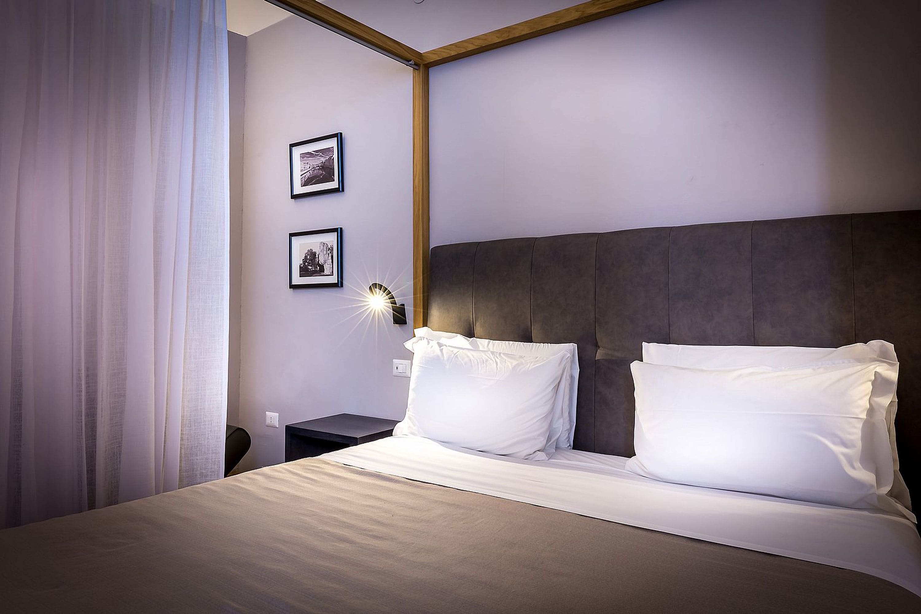 A neatly made bed with white linens and a headboard, a bedside table with a lamp, and two framed pictures on the wall.