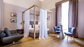 Ein modernes Hotelzimmer mit Himmelbett, einer Couch, einem kleinen Tisch mit Pflanze und einem Sessel.
