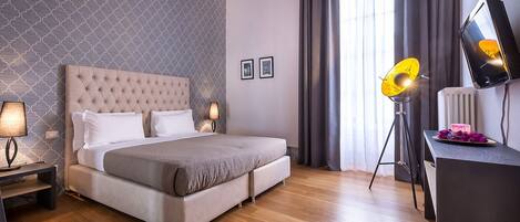 A modern bedroom with a tufted headboard, a large bed, a desk with a lamp, and a view of the outdoors.