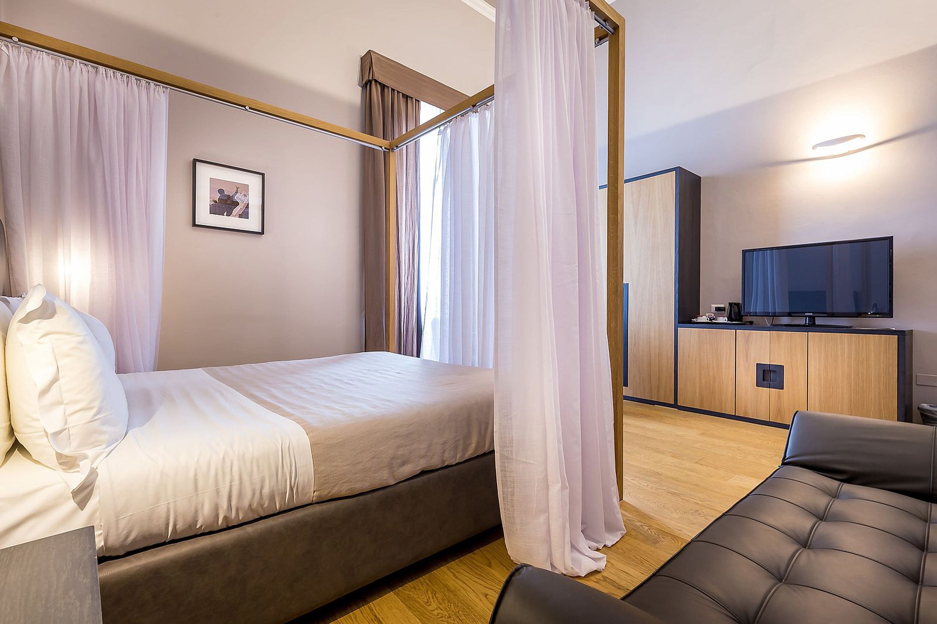 A modern hotel room with a bed, a sofa, a TV, and a wooden cabinet.