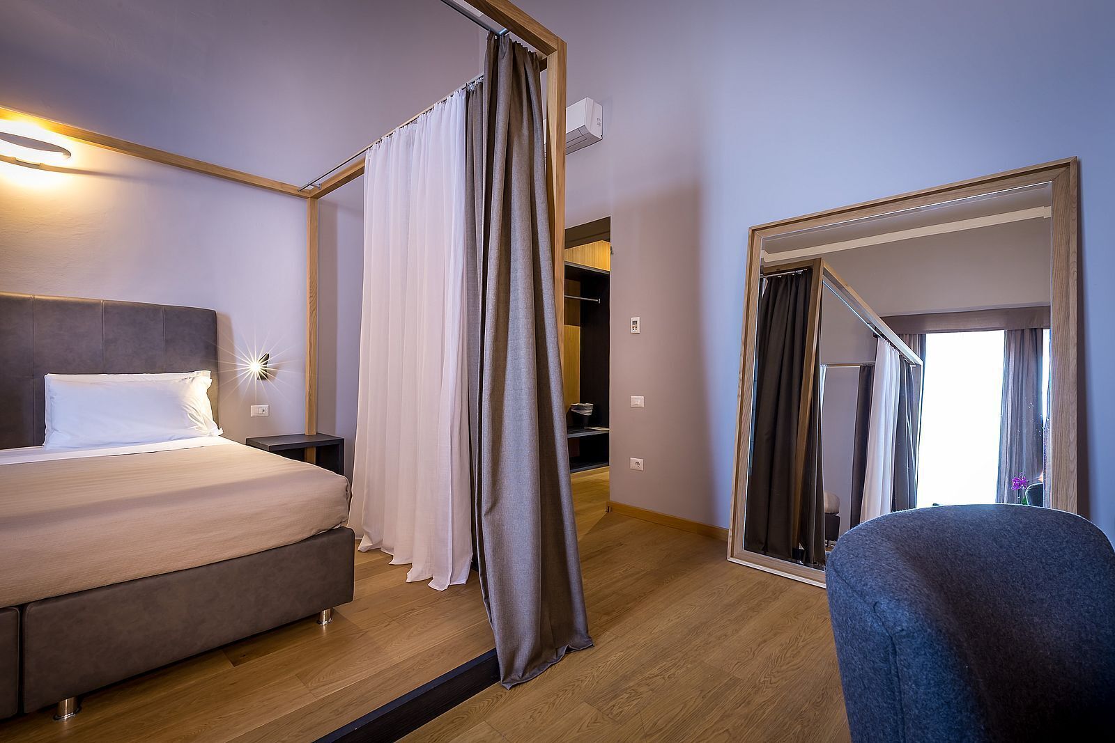 A hotel room with a bed, a bedside table, a mirror, and a view of a hallway.