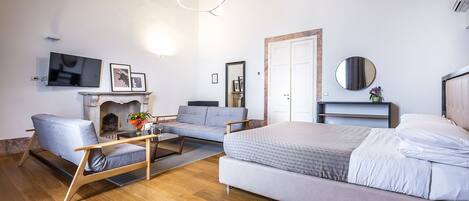 Un dormitorio moderno con una cama grande, un sofá, una silla de madera, una chimenea y un televisor.