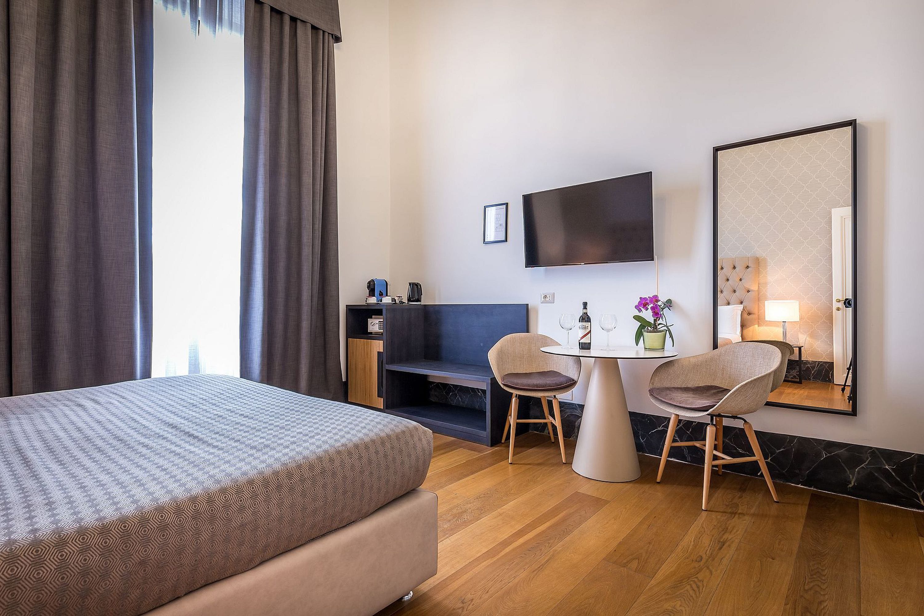 A hotel room with a bed, a desk, two chairs, a TV, and a mirror.
