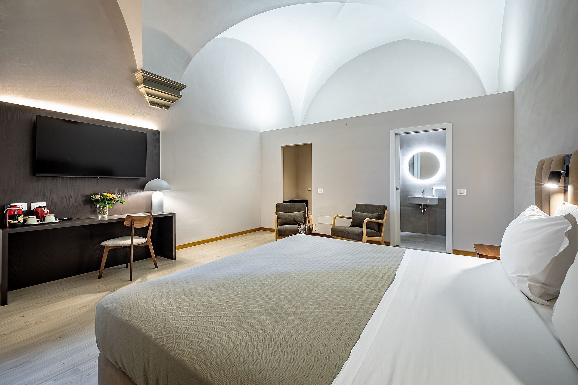 Habitación de hotel con una cama grande, un escritorio con televisor de pantalla plana, dos sillones, un sofá y un baño con espejo y lavamanos.