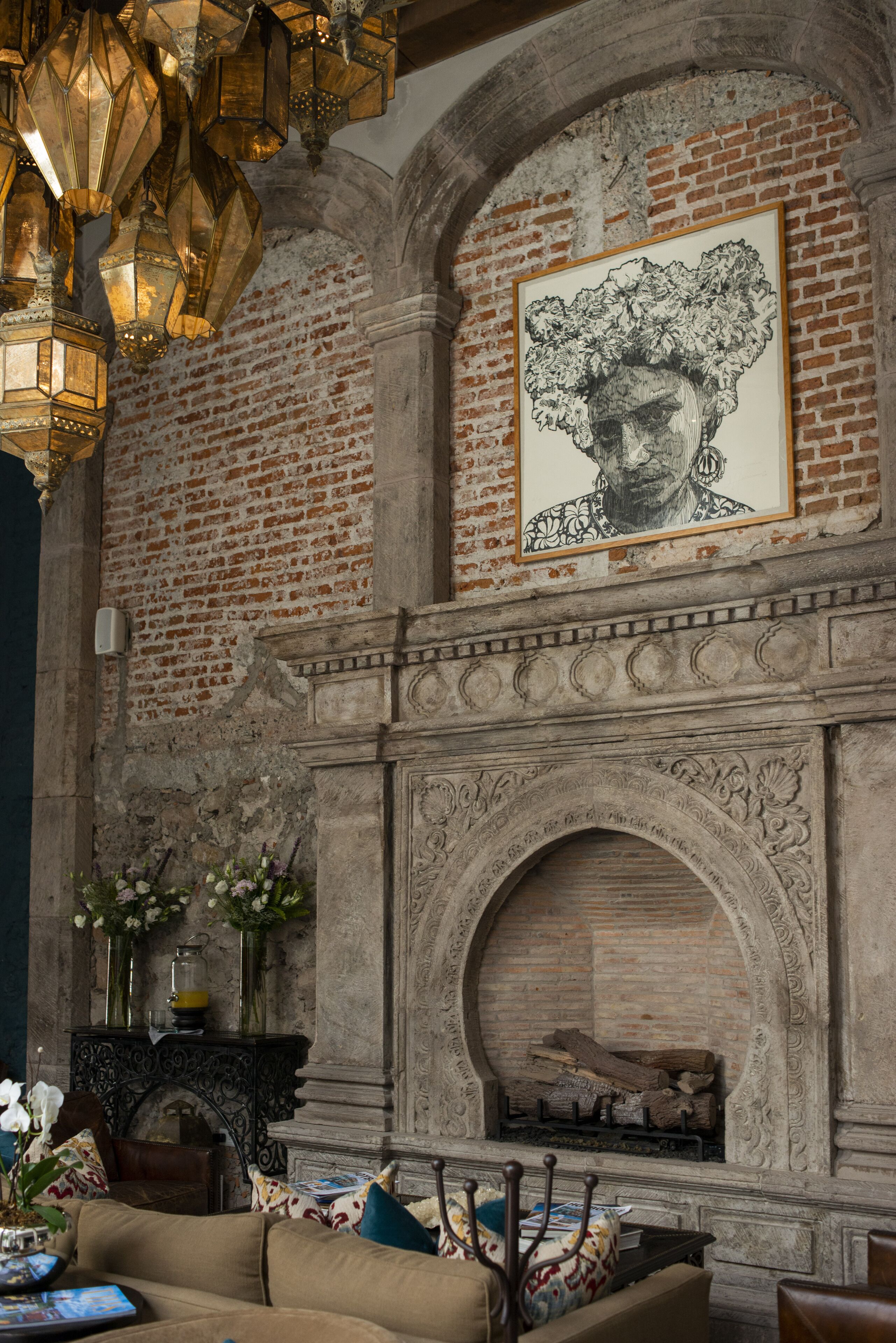 A room with a brick fireplace, a framed artwork above it, and a chandelier.