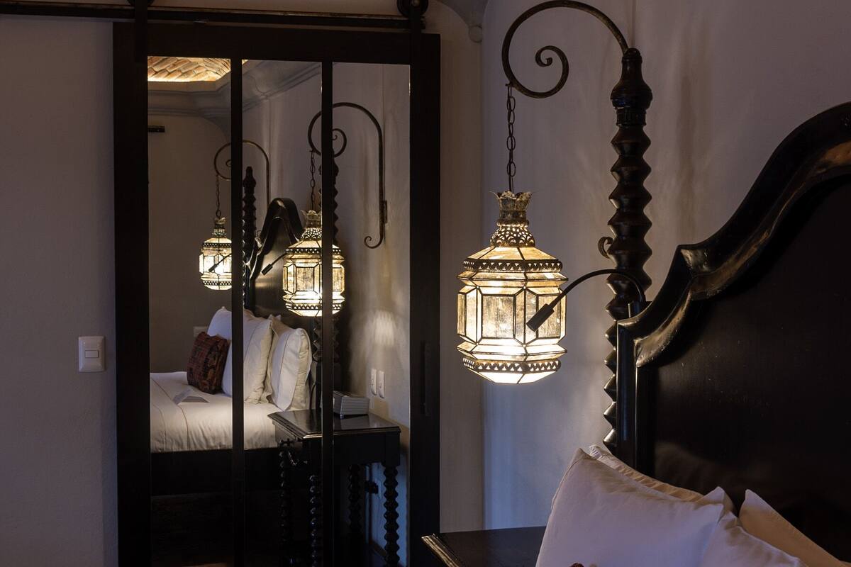 Una habitación de hotel con una cama grande, un espejo, una mesita de noche y faroles colgantes.
