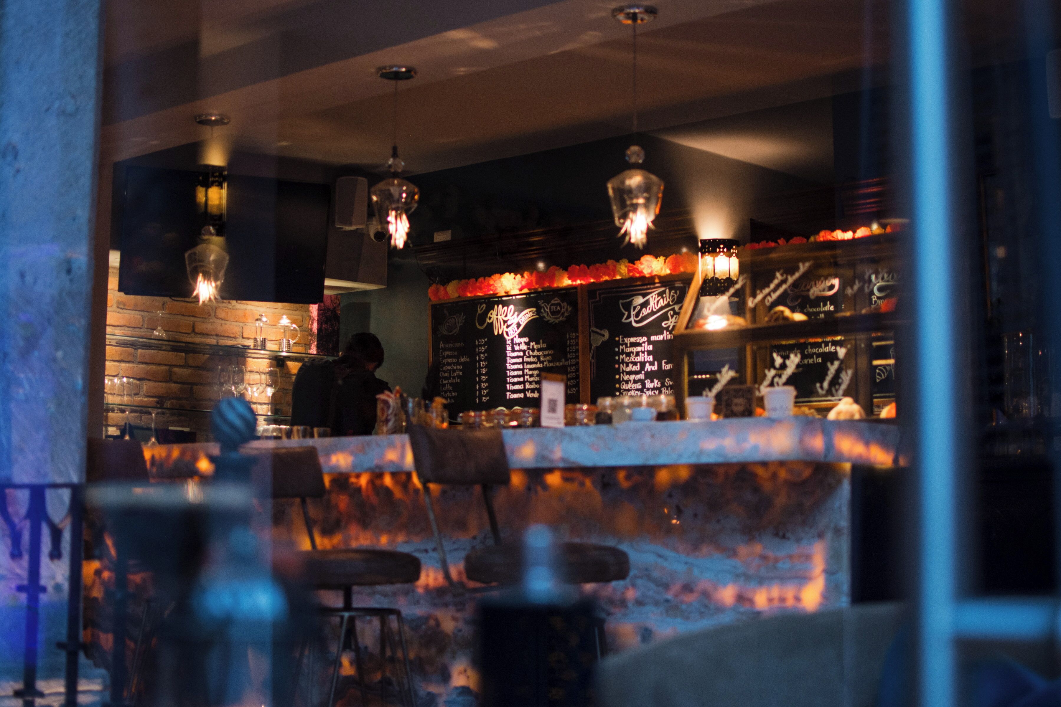 A bar area with a brick wall, hanging lights, and a menu board.