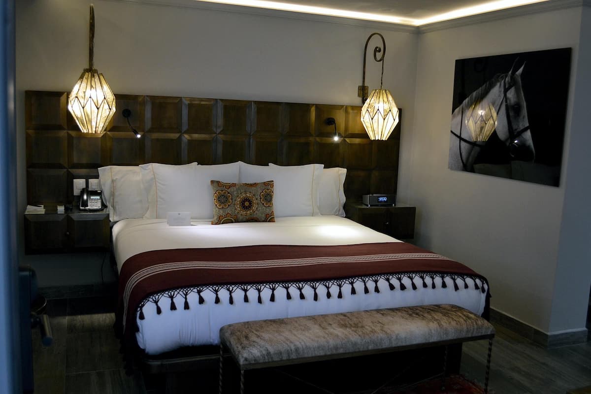 Un dormitorio de hotel moderno con una cama grande, dos lámparas de noche, una mesita de noche y una obra de arte colgada en la pared.