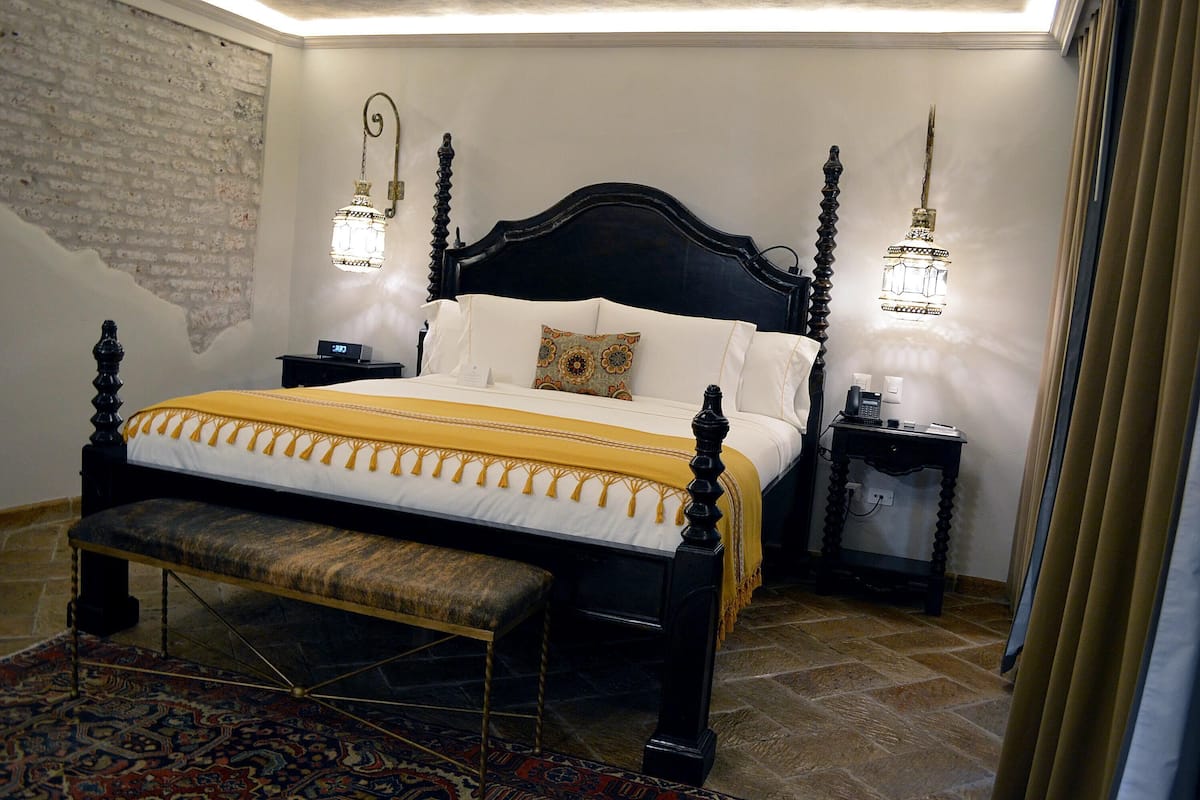 Un dormitorio con cama con dosel, un banco, una mesita de noche y una lámpara fijada a la pared.