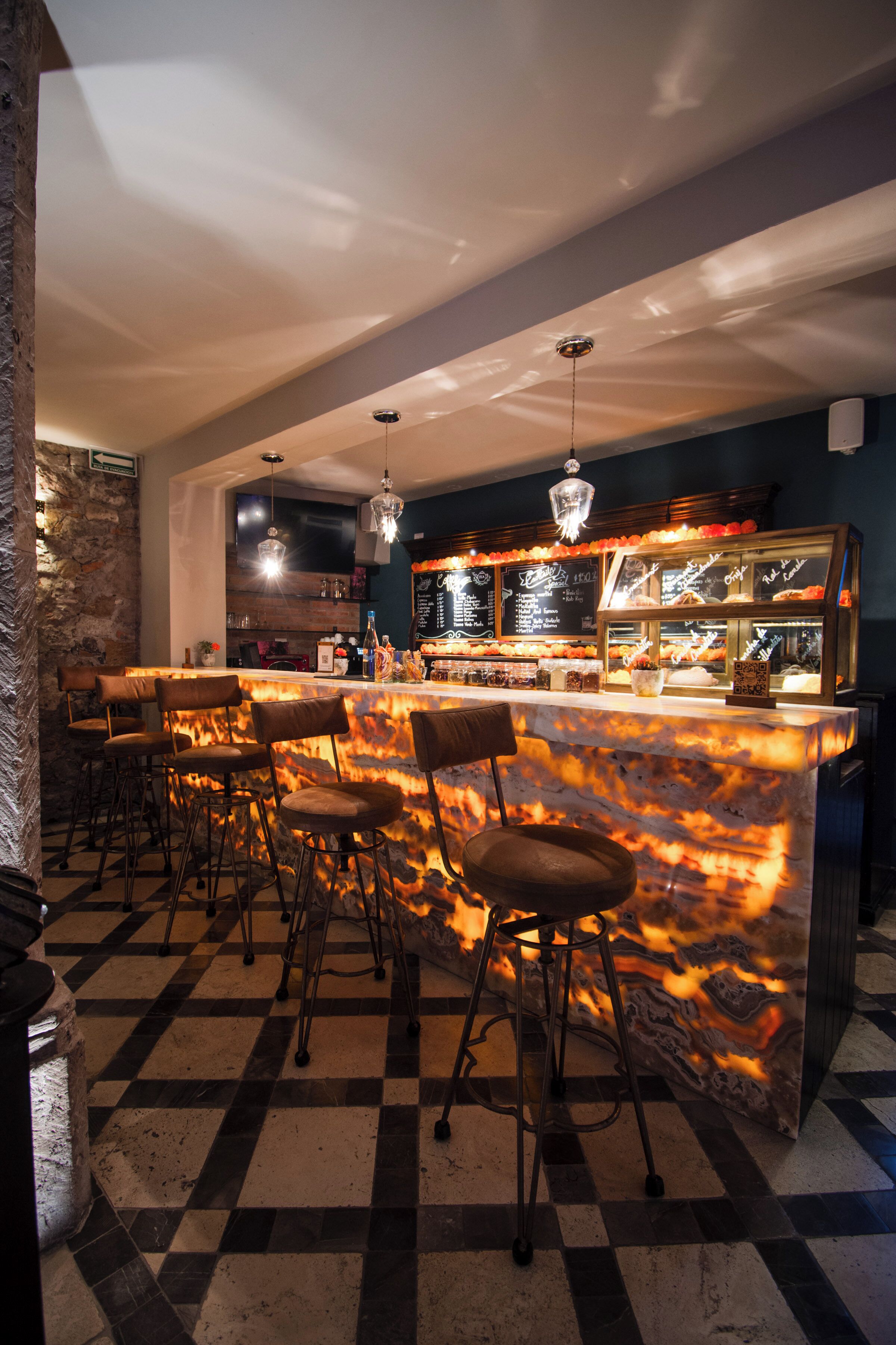 A bar area with a checkered floor, bar stools, a marble bar counter, and a hanging light fixture.