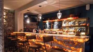 A bar area with a checkered floor, bar stools, a marble bar counter, and a hanging light fixture.
