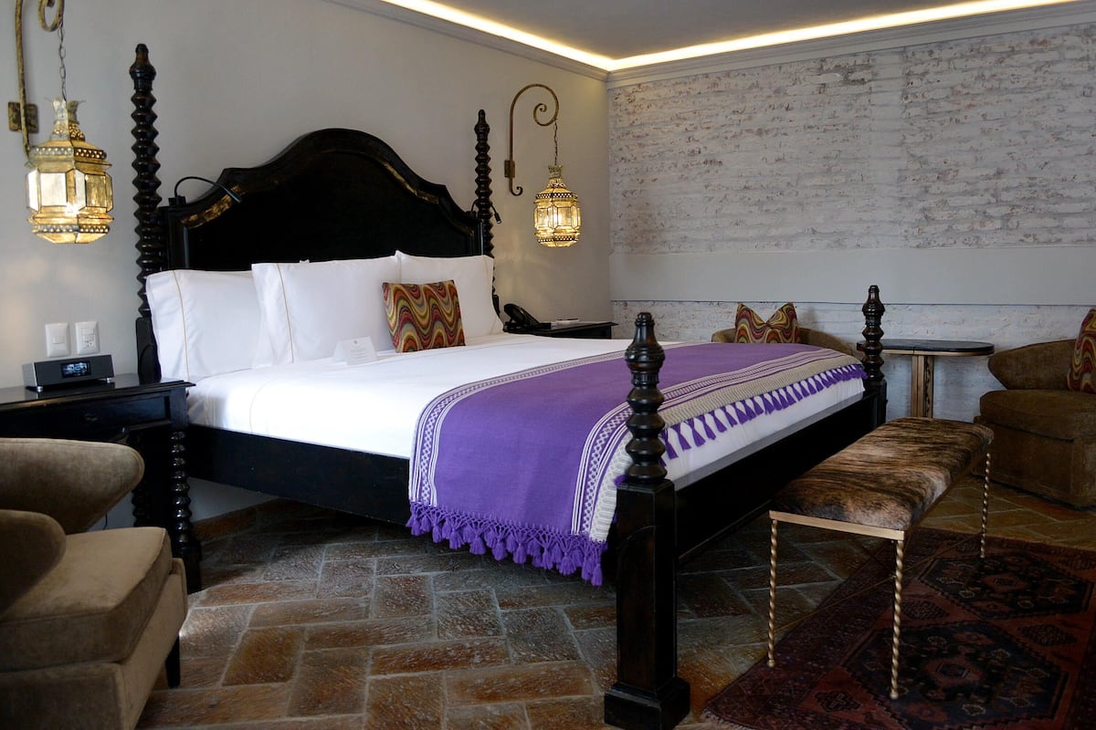 Una cama bien hecha con cabecera, una mesita de noche, una silla y un banco.