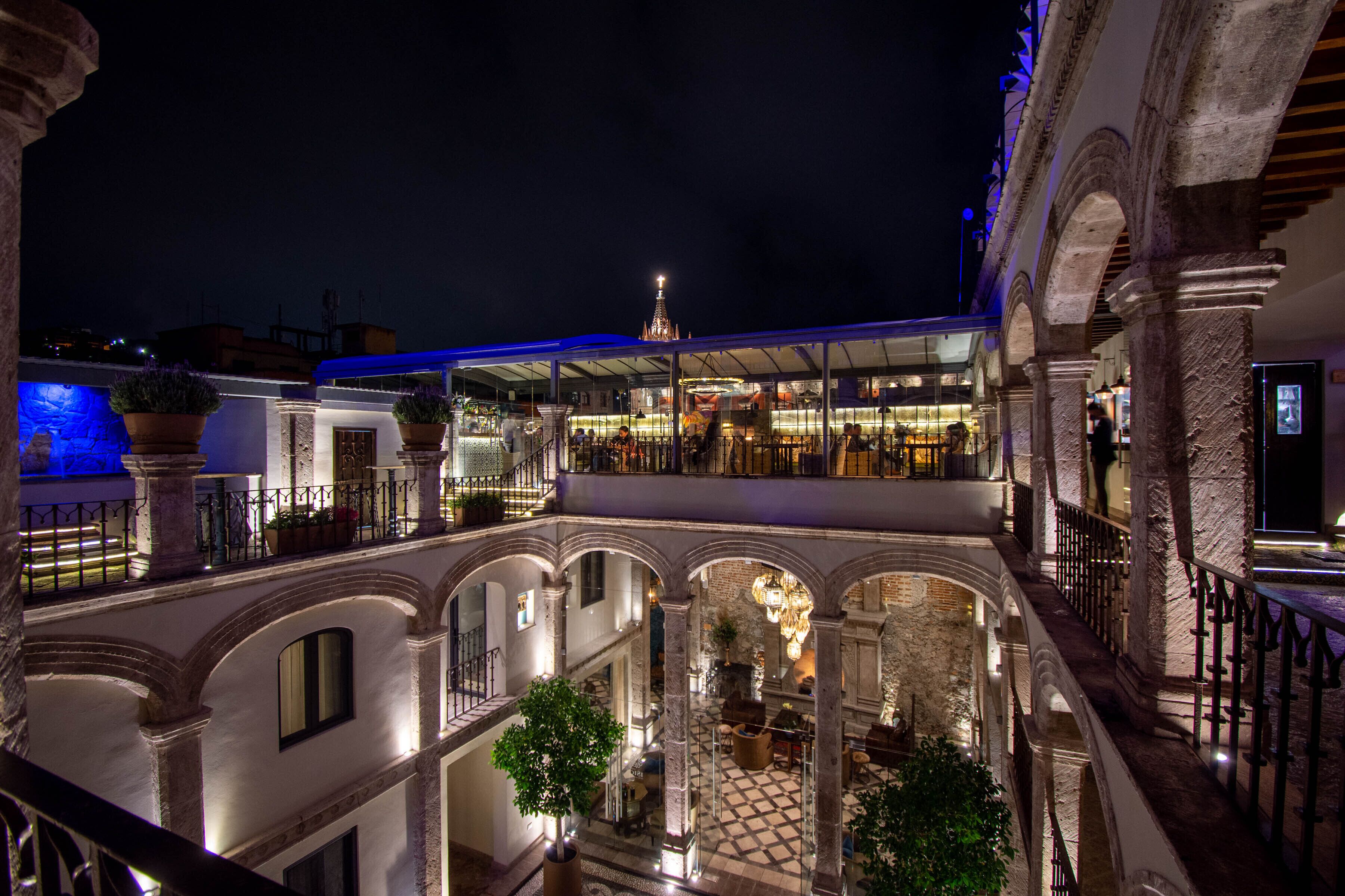 Un patio de varios niveles con arcos, una fuente central y una zona de restaurante con mesas al aire libre.