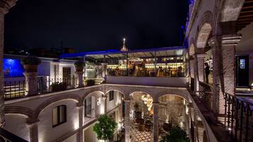 Un patio de varios niveles con arcos, una fuente central y una zona de restaurante con mesas al aire libre.