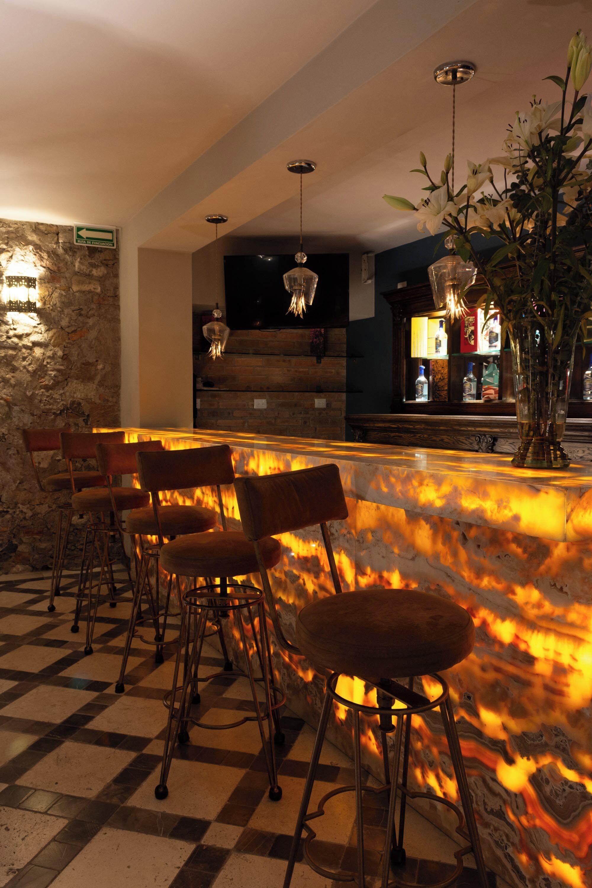 Zona de bar con mostrador de mármol, taburetes y una planta decorativa.