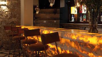 Zona de bar con mostrador de mármol, taburetes y una planta decorativa.
