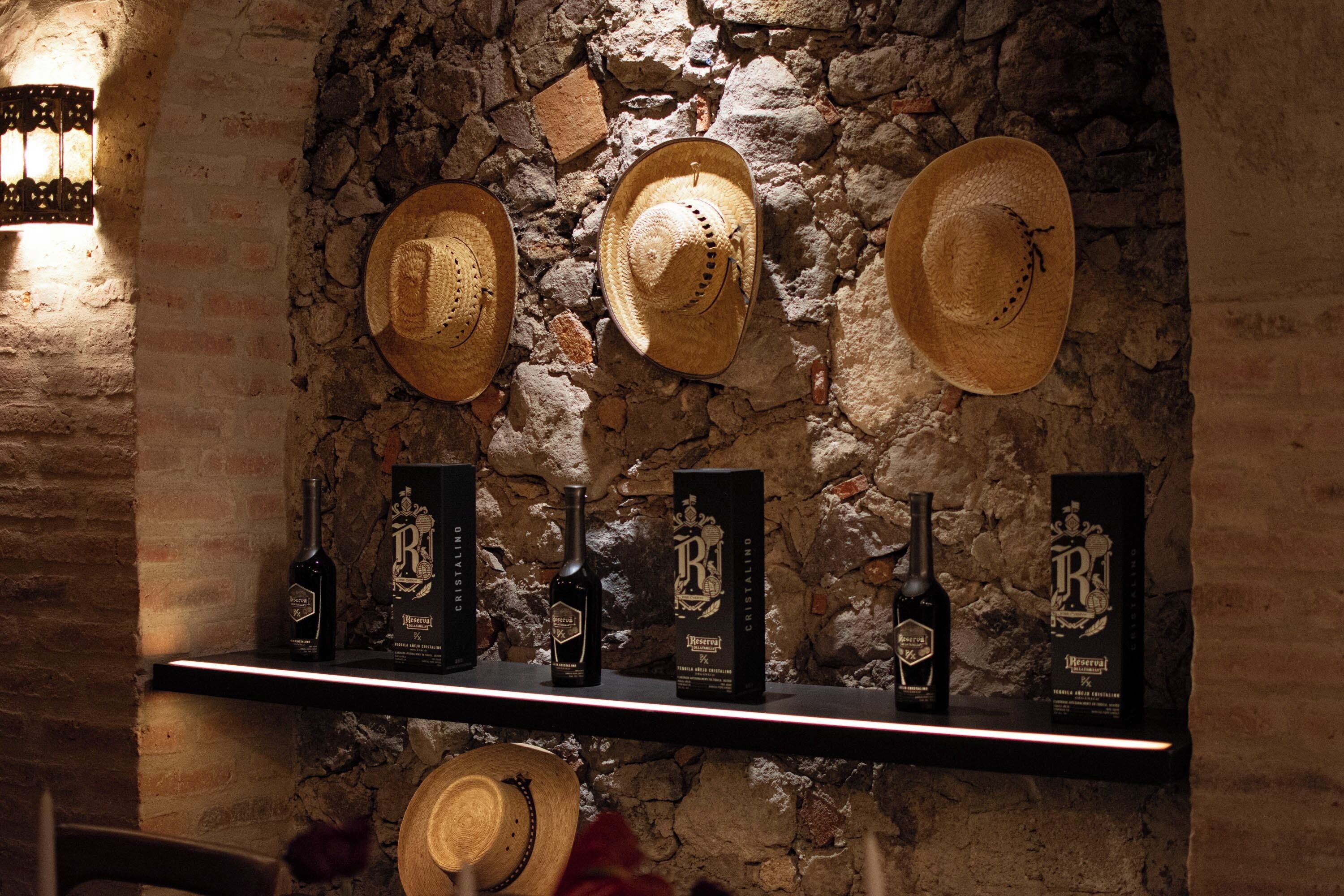 Un estante con sombreros y botellas frente a una pared de piedra.
